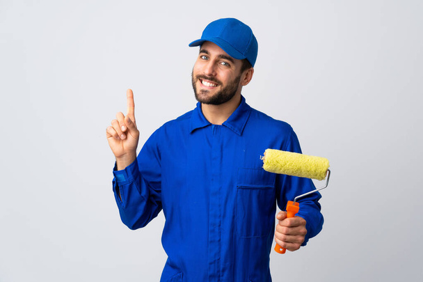 Painter man holding a paint roller isolated on white background showing and lifting a finger in sign of the best - Foto, imagen