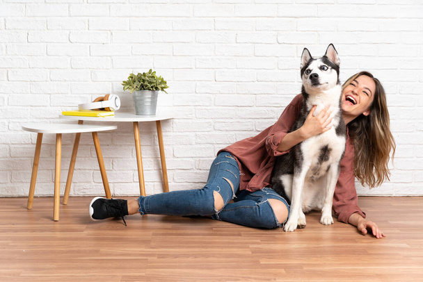 Young pretty woman with her husky dog sitting in the floor at indoors - Photo, Image