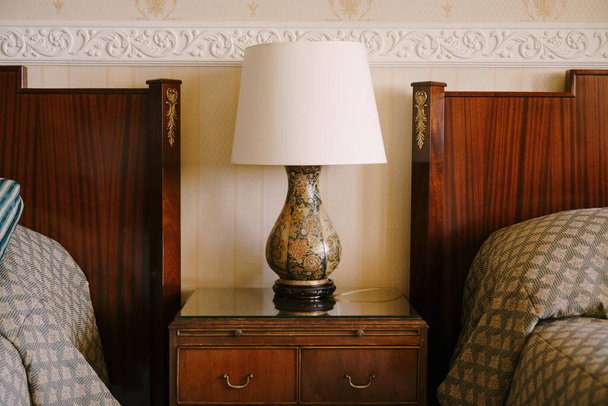 Nachttischlampe auf dem Nachttisch. Raffiniertes und reiches Interieur. Nachttisch aus Holz neben zwei Betten. - Foto, Bild