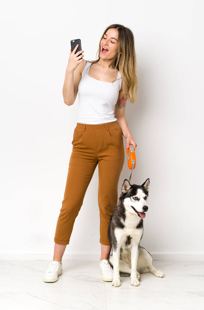 A full length young pretty woman with her dog with phone in victory position - Фото, зображення