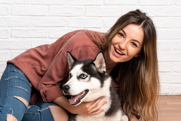 Young pretty woman with her husky dog sitting in the floor at indoors - Fotografie, Obrázek