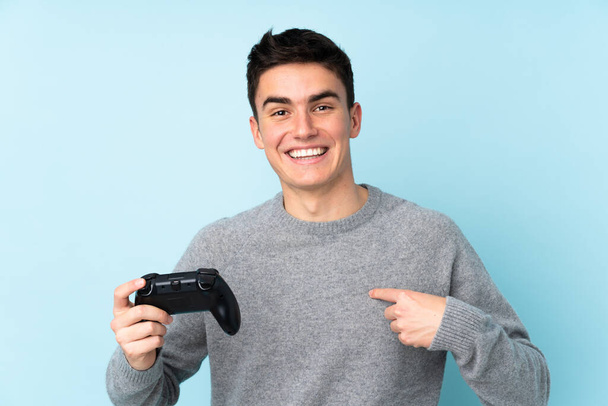 Mavi arka planda izole edilmiş bir bilgisayar oyunu kontrolörüyle oynayan beyaz bir genç. - Fotoğraf, Görsel