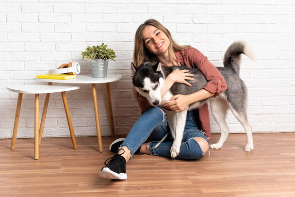 Young pretty woman with her husky dog sitting in the floor at indoors - Photo, Image
