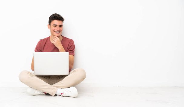 Teenager sitzt mit Laptop auf dem Boden und schaut zur Seite - Foto, Bild