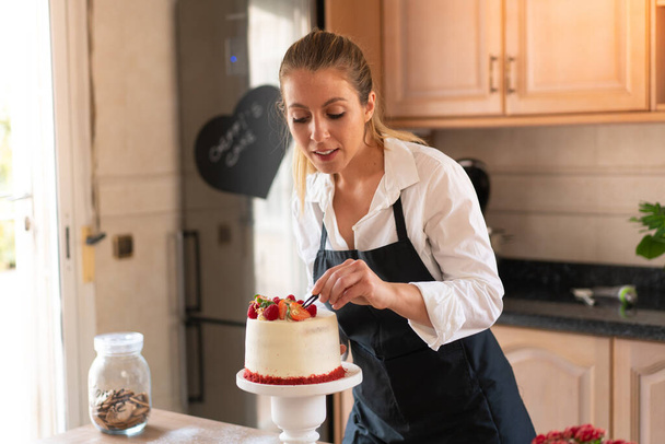 キッチンで伝統的な赤いベルベットのケーキを調理する若いペストリーシェフ - 写真・画像