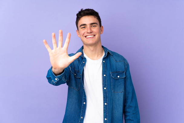 Adolescente caucasiano bonito homem isolado no fundo roxo contando cinco com os dedos - Foto, Imagem