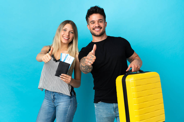 Young caucasian couple going to travel isolated on blue background giving a thumbs up gesture because something good has happened - Φωτογραφία, εικόνα