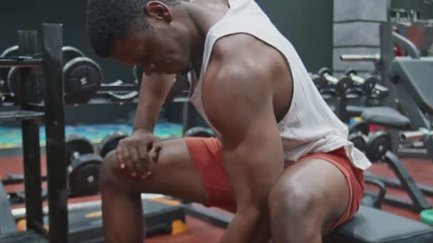 Young muscular afro powerful man lifts dumbbell sits on a bench. - Footage, Video
