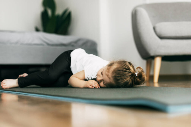 Маленька дівчинка лежить на килимку для йоги в спальні і спить після гри
 - Фото, зображення