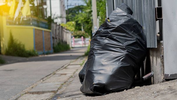Una bolsa de basura negra colocada junto a ella estaba goteando en la calle. - Foto, Imagen