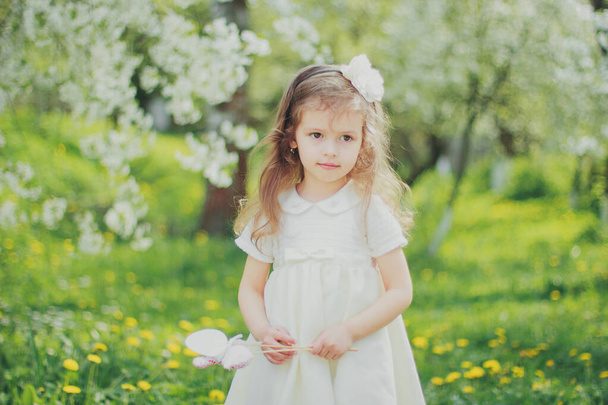Dívka v bílém držení velikonoční hračka vejce na tyčinky v jarní cherry zahradě - Fotografie, Obrázek