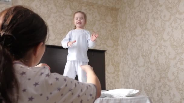 Happy daughter jumps out of bed to her mother in her arms and hugs her. Mother plays with her baby in morning. Family is having fun at home. Active family vacation at home. Happy healthy childhood - Footage, Video