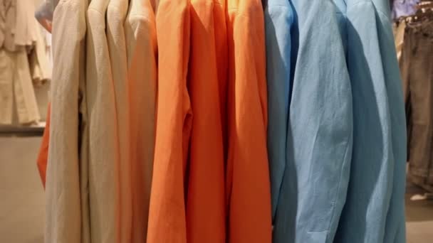 A woman walks past a stand with colorful jackets on hangers, and runs her hand over them. Close up. Real time. The concept of consumerism and shopping. - Footage, Video