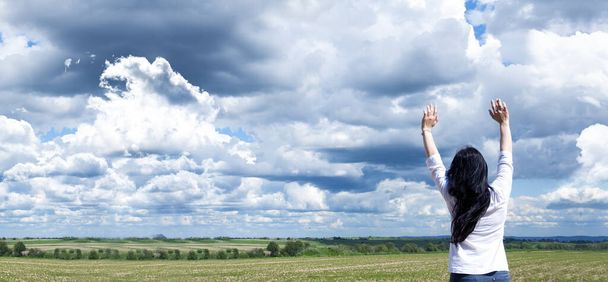 腕を上げた若い女の子。青空と雲の背景を背景に。喜べ。神への祈りと崇拝. - 写真・画像