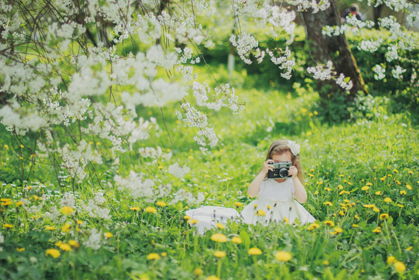 Κοριτσάκι σε λευκό φόρεμα κρατώντας φωτογραφική μηχανή φιλμ στον κήπο της άνοιξης κεράσι - Φωτογραφία, εικόνα