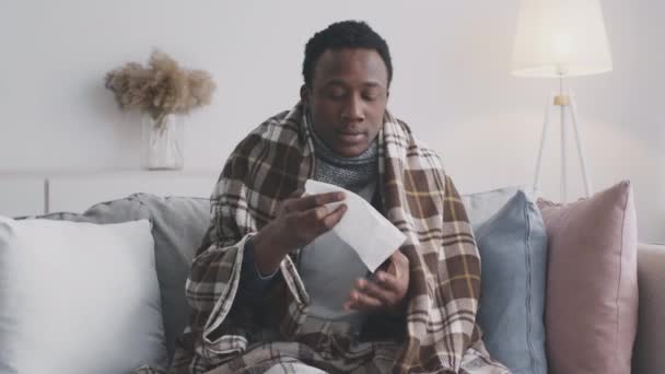 Sintomas de gripe e frio. Jovem afro-americano sofrendo de gripe, espirros e assoprando o nariz em casa - Filmagem, Vídeo