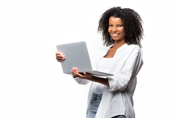 Χαμογελώντας αφροαμερικανή γυναίκα κρατώντας φορητό υπολογιστή απομονωμένο σε λευκό  - Φωτογραφία, εικόνα