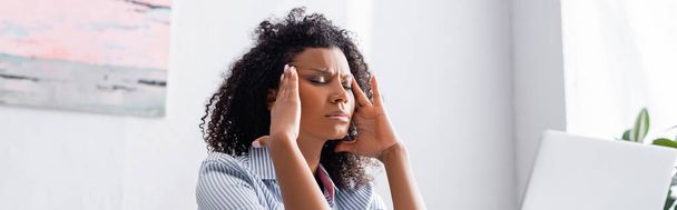 Африканская американка страдает от головной боли возле ноутбука на размытом переднем плане, баннер  - Фото, изображение