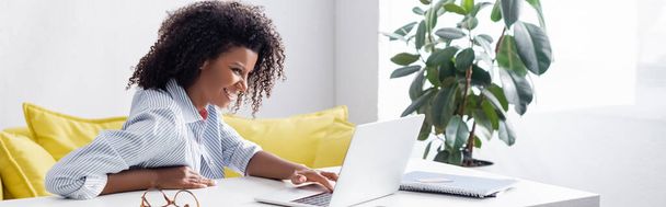 Freelance afro-americano sorridente che utilizza laptop vicino a carta di credito e notebook, banner  - Foto, immagini