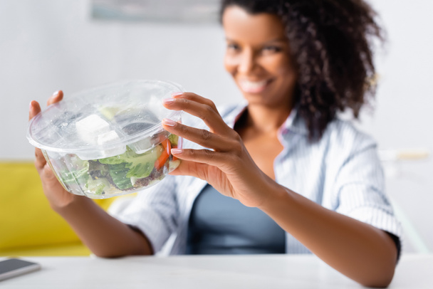 Salade à emporter entre les mains d'une femme afro-américaine sur fond flou  - Photo, image