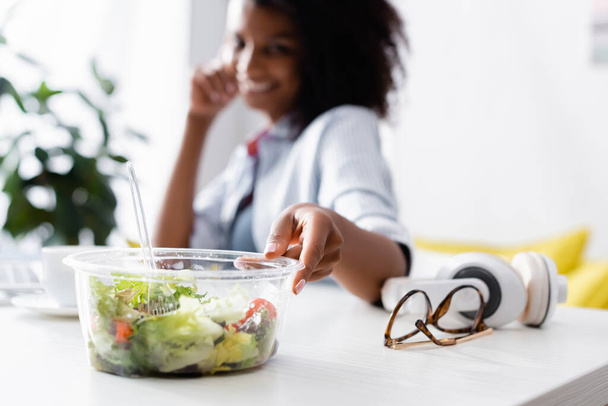 Takeaway salada perto de óculos e mulher americana africana no fundo borrado  - Foto, Imagem