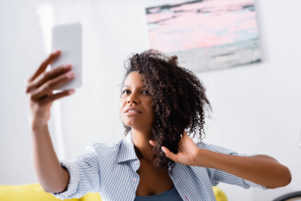 Κέρλι αφροαμερικανή γυναίκα που παίρνει selfie στο κινητό σε θολή πρώτο πλάνο  - Φωτογραφία, εικόνα