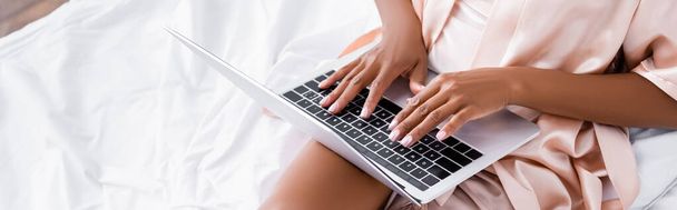 Cropped view of african american freelancer using laptop on bed, banner  - Photo, Image
