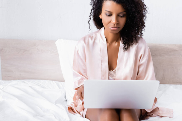 Африканська американка тримає ноутбук на розмитому передньому плані на ліжку  - Фото, зображення