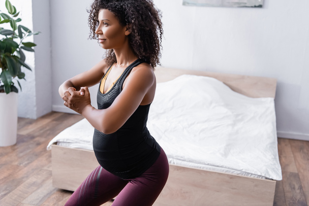 Embarazada mujer afroamericana haciendo ejercicio en el dormitorio  - Foto, Imagen