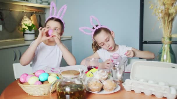 Funny little sisters wearing bunny ears painting eggs on Easter day - Footage, Video