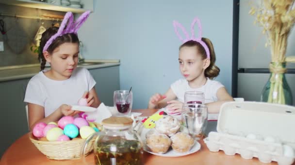 Zabawne siostrzyczki w króliczych uszach malujące jajka w Wielkanoc - Materiał filmowy, wideo
