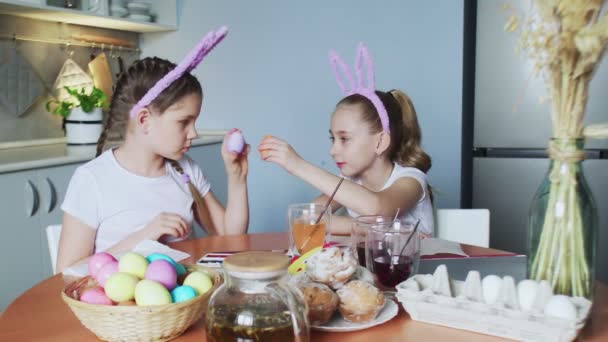 Hyvää pääsiäistä. Kaksi siskoa maalaa pääsiäismunia. Onnelliset perheen lapset valmistautuvat pääsiäiseen. Söpö pieni lapsi tyttö yllään pupu korvat eivät munat taistella kameran - Materiaali, video