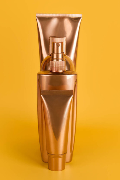 Golden bottles, cosmetic products on yellow background. Luxury beauty style. Gold cosmetic containers. Mockup bottles, cosmetics branding, hair or body care concept - Photo, Image