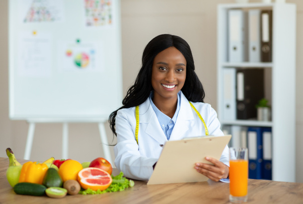 Positiivinen musta ravitsemusterapeutti leikepöydällä luoda terveellisen aterian suunnitelma potilaalle klinikalla, tyhjä tila - Valokuva, kuva