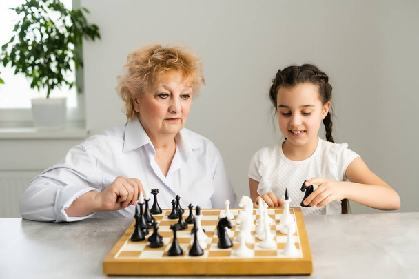 Boldog lány, nagymama ül az asztalnál és sakkozik - Fotó, kép