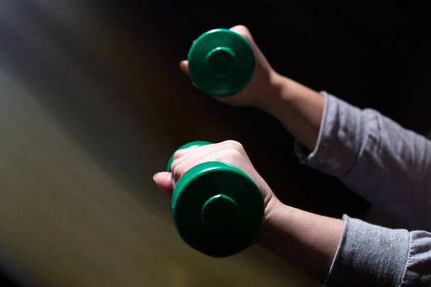 Woman's hands doing exercises with dumbbells on black background with copy space. - Photo, Image