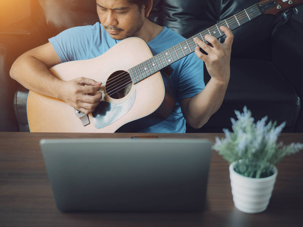 Muž hrající na kytaru ve svém pokoji. Šťastný mladý muž hraje na kytaru na pohovce v obývacím pokoji, relaxační víkend doma. - Fotografie, Obrázek