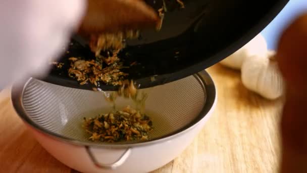 Zeef de gefrituurde knoflook en gehakte rozemarijnbladeren door een zeef. Proces van het koken van perfecte oven geroosterde aardappelen - Video