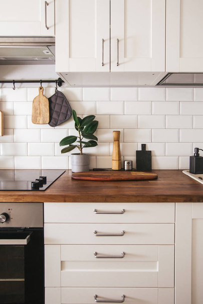 Kitchen brass utensils, chef accessories. Hanging kitchen with white tiles wall and wood tabletop.Green plant on kitchen background vertical side view - Φωτογραφία, εικόνα