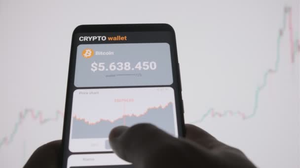  Okostelefon mobilalkalmazás cryptocurrency pénztárcával. Egy férfi elemzi a bitcoin ártáblázatát egy mobil alkalmazásban, és bitcoint vásárol. A cryptocurrency kereskedés fogalma - Felvétel, videó