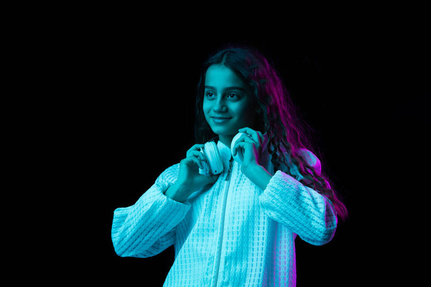 Νεαρή όμορφη κοπέλα με ακουστικά που απομονώνονται σε σκούρο φόντο σε νέον φως - Φωτογραφία, εικόνα