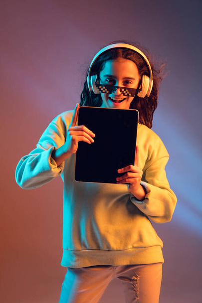 Young beautiful girl in headphones isolated on light background in neon light - Photo, Image