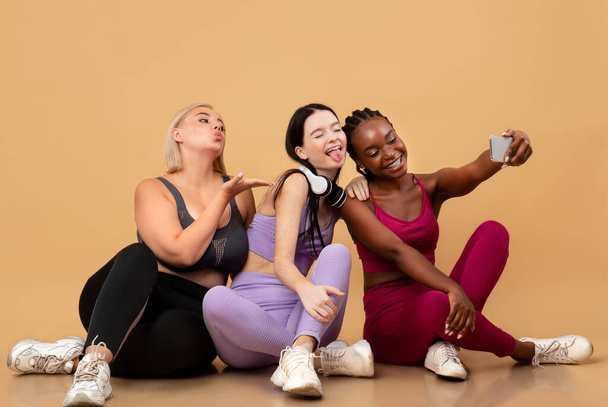 Fröhliche multiethnische Frauen in Sportkleidung, die nach dem Training Selfie auf dem Smartphone machen - Foto, Bild