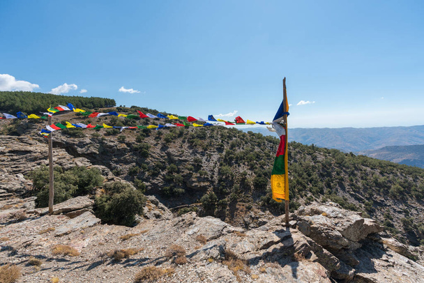 Tibetan flags in Sierra Nevada in southern Spain, it is a rocky area, there is a pine forest and bushes, the sky is clear - Photo, Image