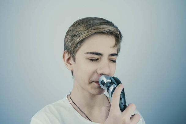 Teenage boy is shaving at first time his mustaches with an electric razor. Young man shaves his face with a electric razor. - Фото, изображение