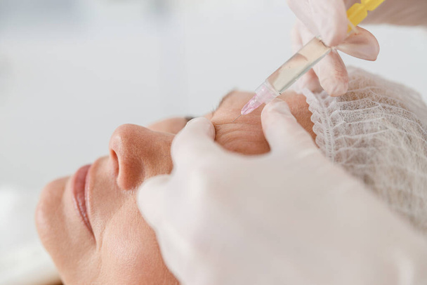Close-up maakt mesotherapie injecties aan een oudere vrouw. Behandeling van een vrouw door een schoonheidsspecialiste voor het aantrekken en gladstrijken van rimpels op de gezichtshuid - Foto, afbeelding