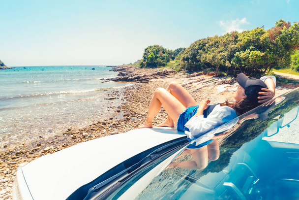 женщина лежит на капоте автомобиля с видом на море летний отдых на пляже копировальное место - Фото, изображение