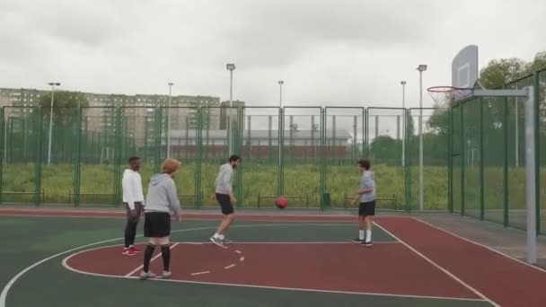 Handheld tiro de rastreamento de jovens homens atirando aros na quadra de basquete ao ar livre no dia sombrio - Filmagem, Vídeo