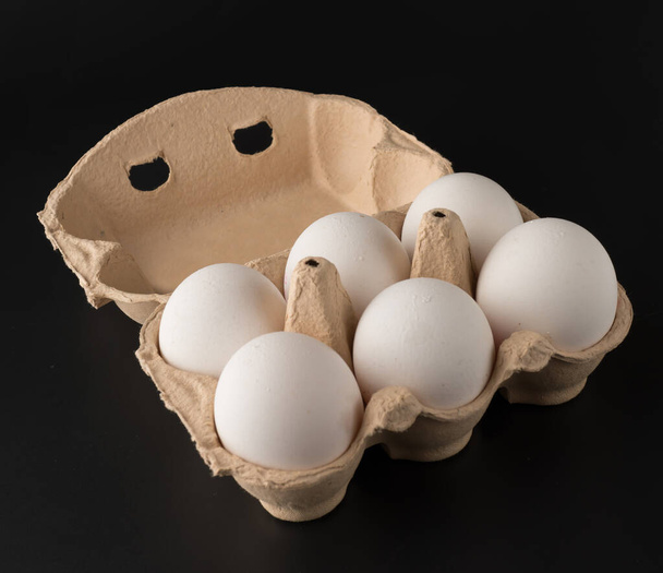 Huevos de pollo, en la cantidad de seis piezas en una bandeja de papel desechable, sobre un fondo negro, aislados - Foto, Imagen