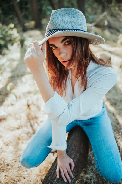 A vertical shot of a sexy stylish female sitting on a tree stump in a forest - Foto, Bild